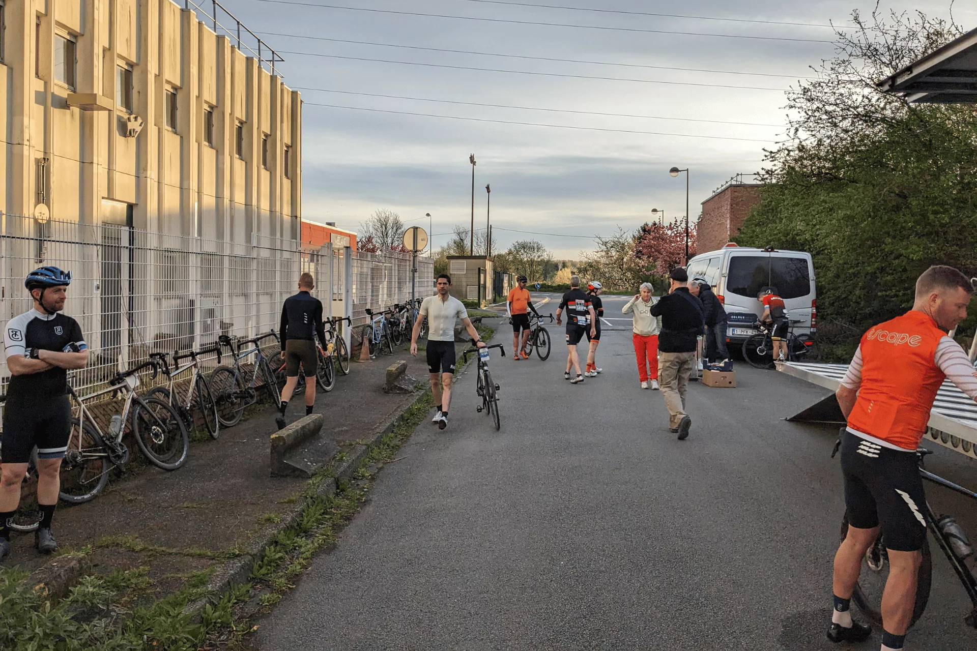 A dozen cyclists unloading bikes from a trailer and milling about