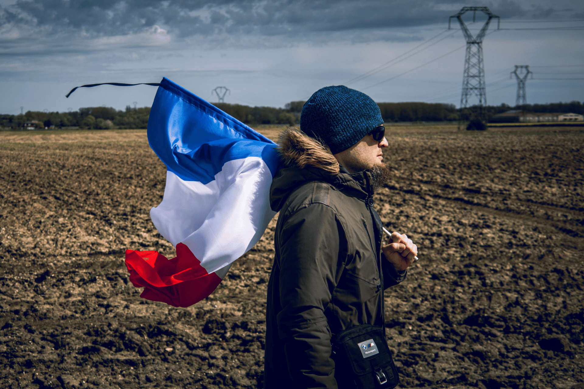 A mann wearing a blue beanie and a winter jacket and carrying a French flag