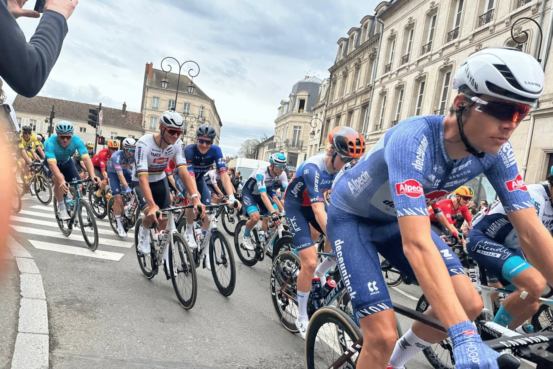 A peloton of road cyclists riding in tight formation through the streets of Compiègne