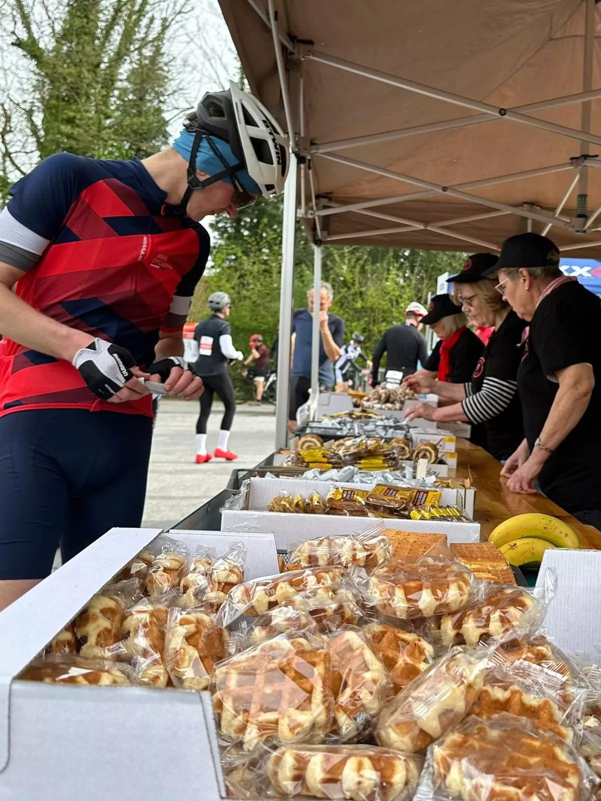 A cyclist perusing trestle tables covered in various pastries and fruit