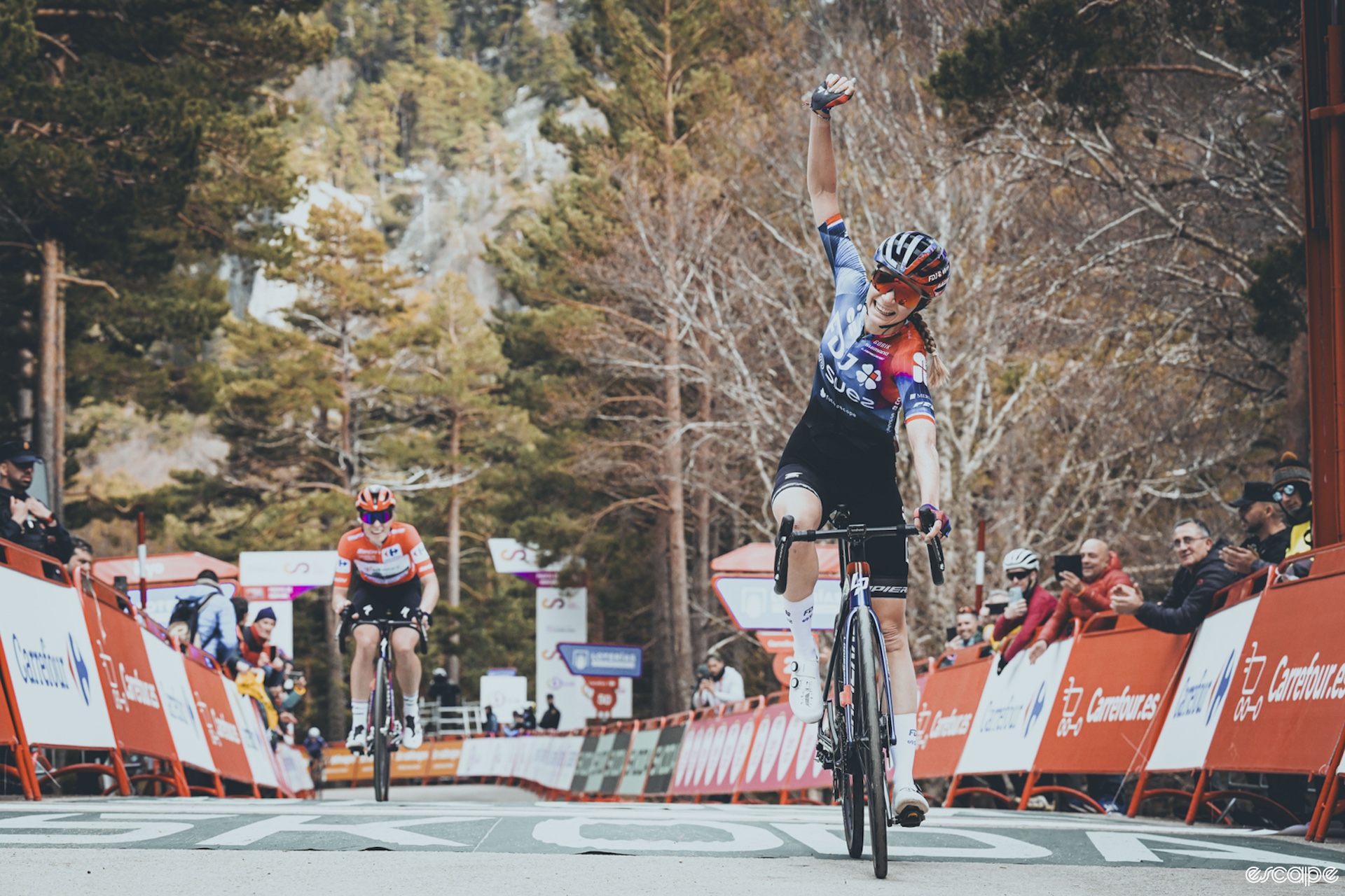 Evita Muzic raises her arm as she wins the sixth stage of La Vuelta, Demi Vollering grimaces in the background.