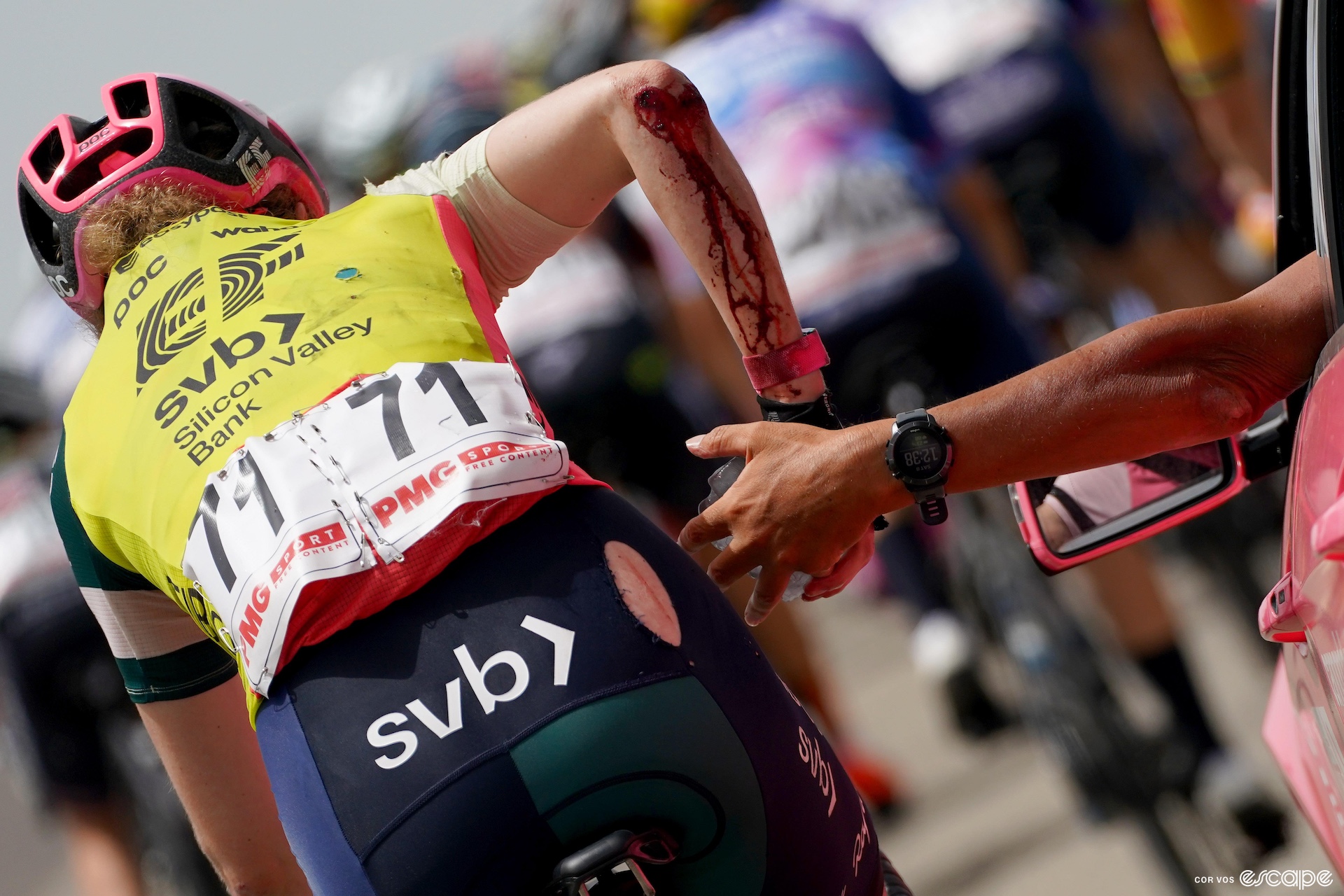Banks pictured from behind, jersey cut and covered in blood as she takes a bottle from the team car