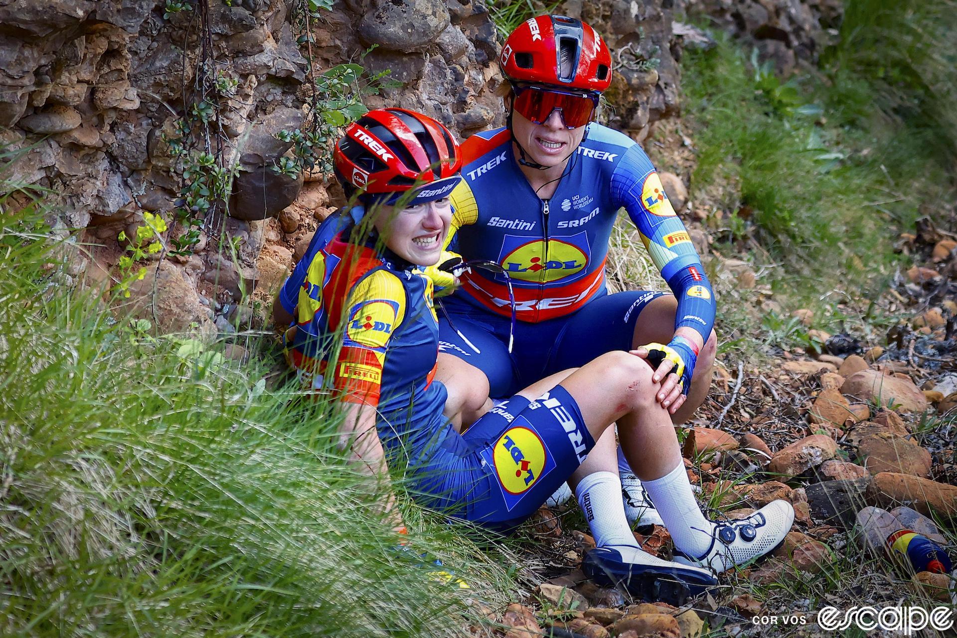Gaia Realini winces in pain as she sits on the side of the road after crashing on stage 5 of La Vuelta Femenina. Her Lidl-Trek teammate Brodie Chapman crouches next to her, taking a watchful approach to her banged-up teammate.