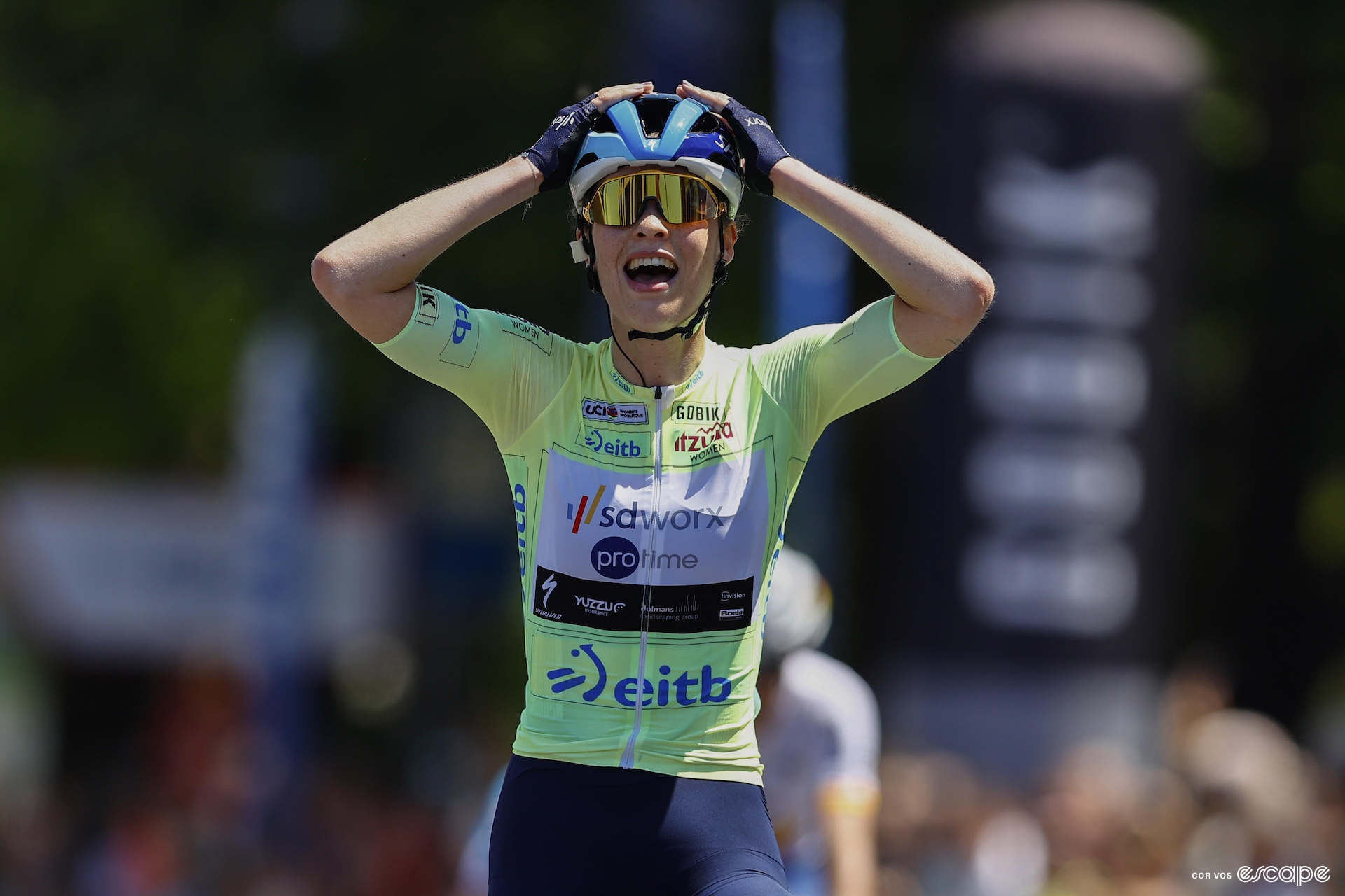 Mischa Bredewold holds her head in her hands in shock as she crosses the finish line of a bike race 
