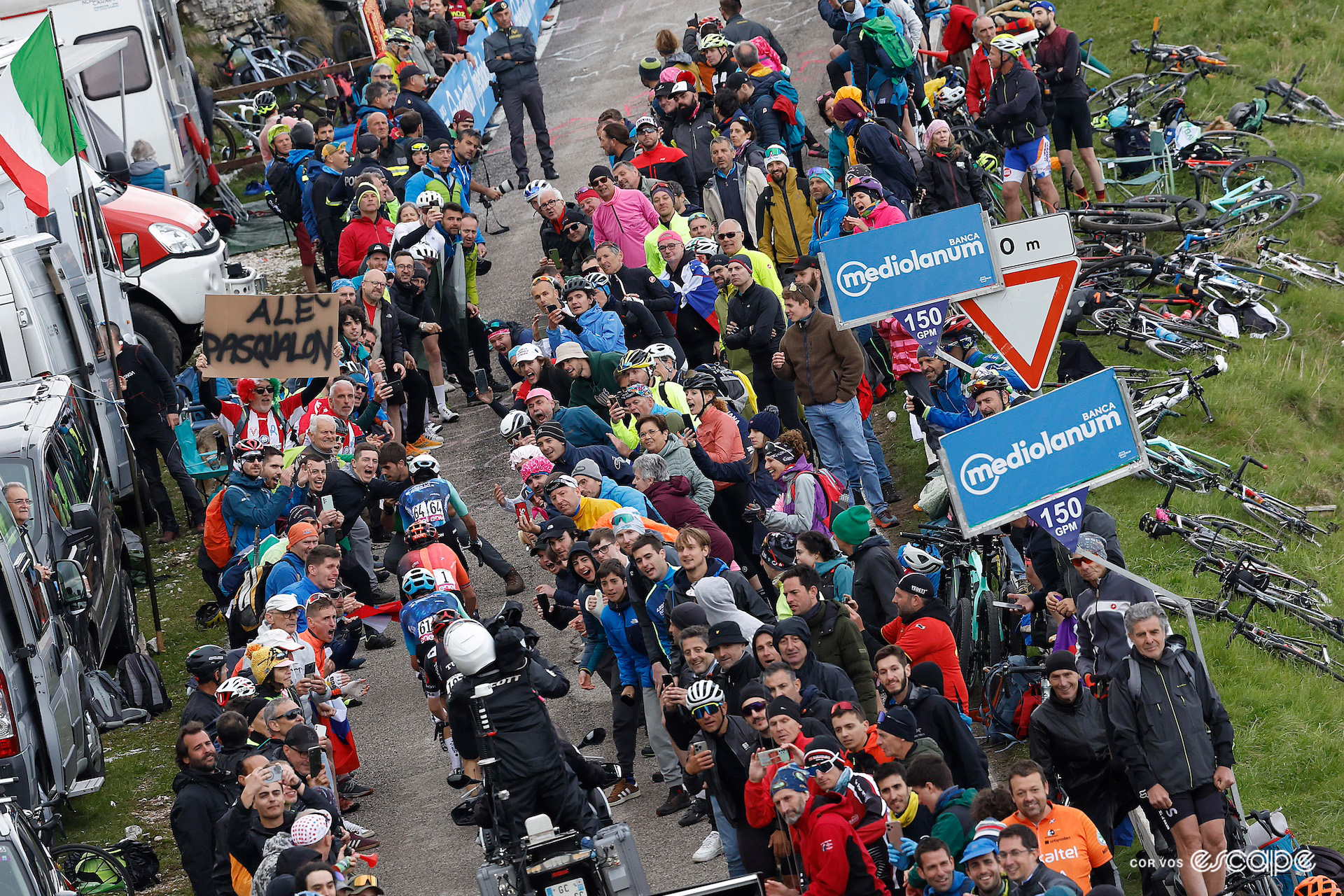 Valentin Paret-Peintre, Geraint Thomas and Ben O'Connor ride up a narrow path through the crowd near the top of the Monte Grappa climb on stage 20 of the 2024 Giro d'Italia.