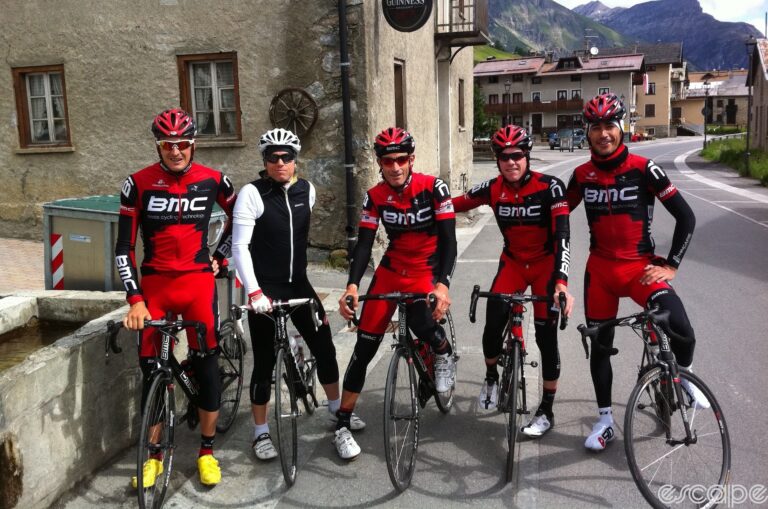 Peredur ap Gwynedd, guitarist for Pendulum, stands with several BMC pros including George Hincapie after riding the Stelvio pass. Perry is dressed in black and white cycling kit in contrast to the BMC riders' mostly red and black kit as they stand over their bikes facing the camera.