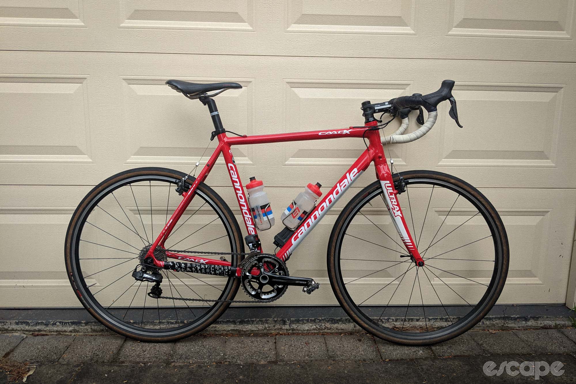 Red Cannondale CAADX leaning against a garage door, with Dura Ace Di2 groupset, cantilever brakes, skinny tyres. 