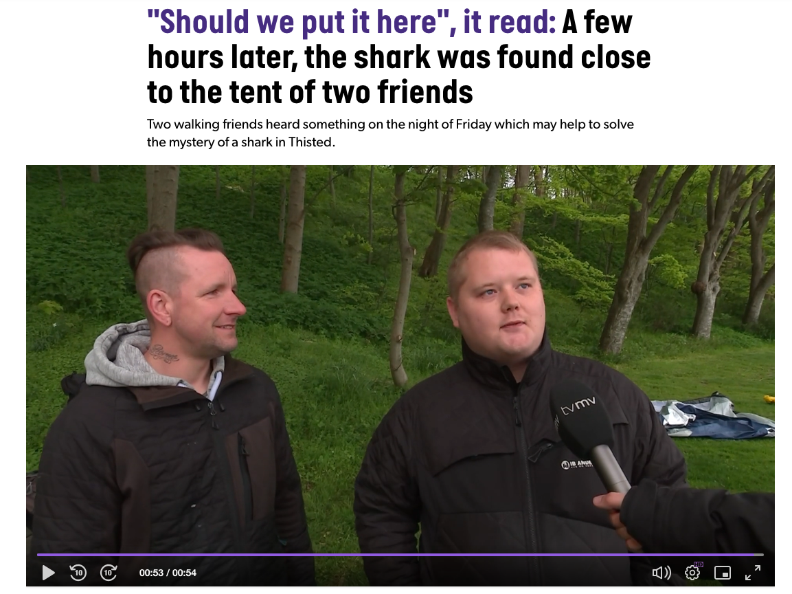 Two Danish men answer questions in an interview, their partially disassembled tent behind them. A microphone is in front on one of their faces. 