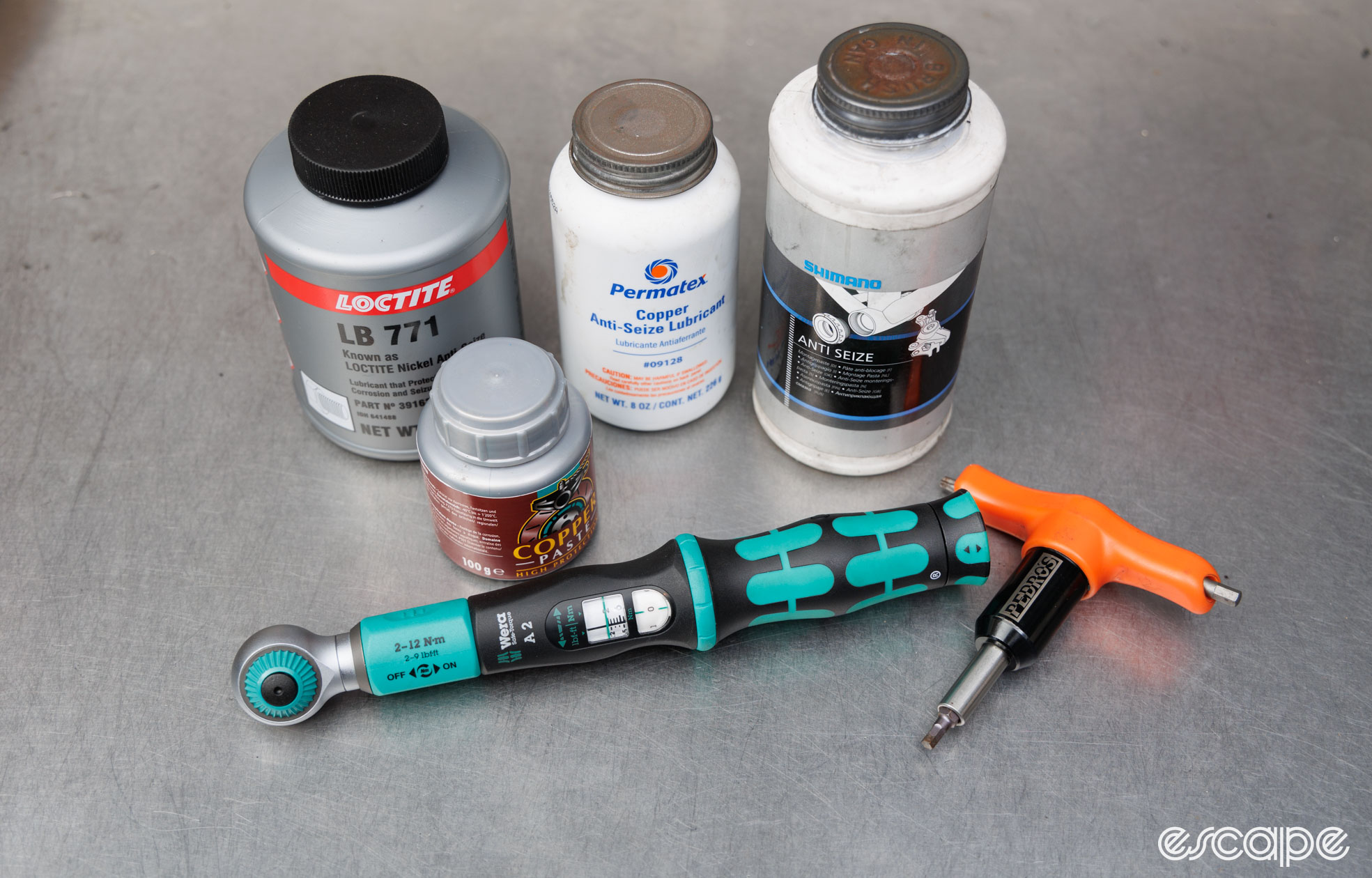 A bunch of anti-seize lubricants sit on a bench with two torque wrenches. 