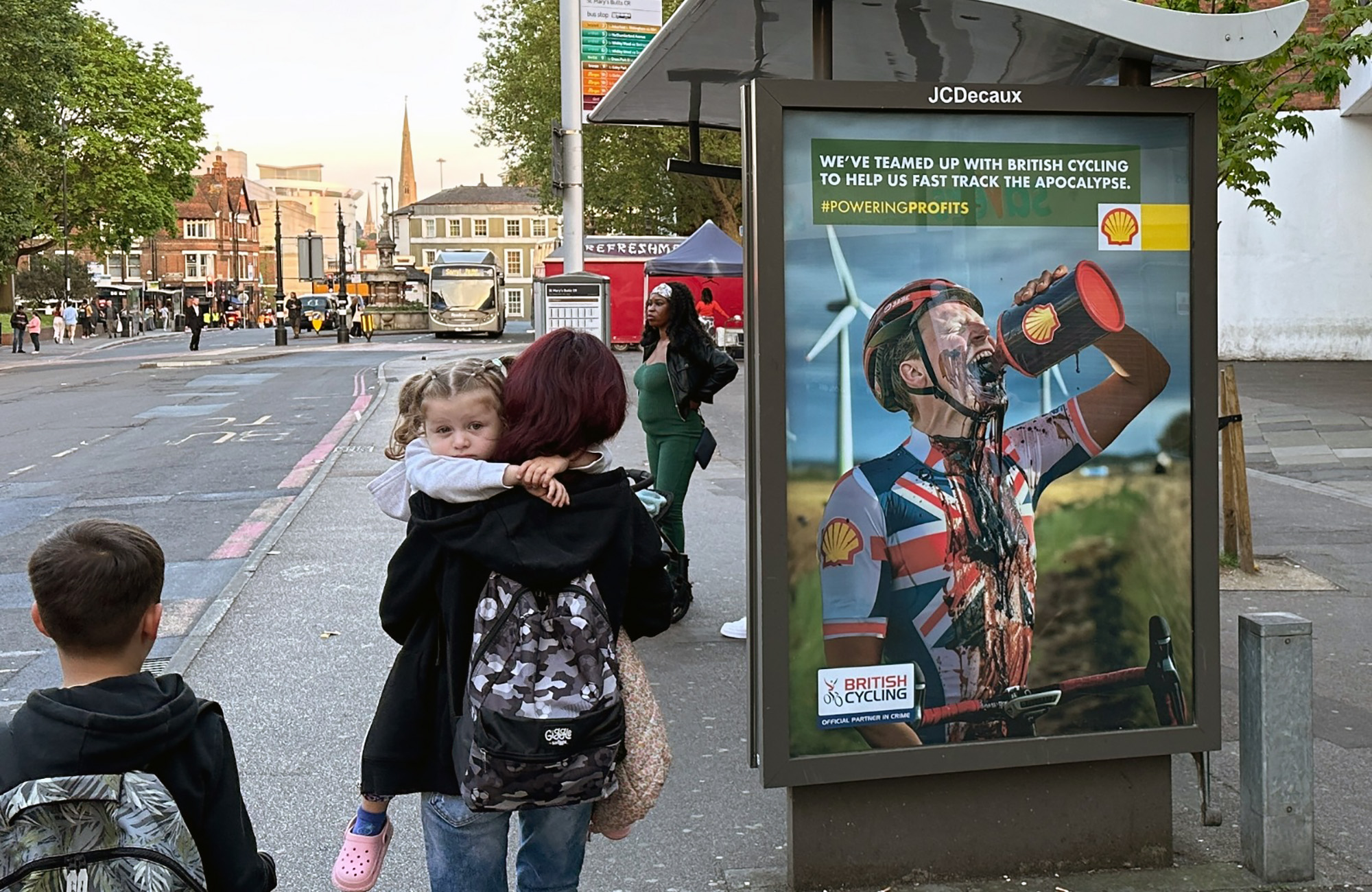 A family walks past a Shell/British Cycling protest poster.
