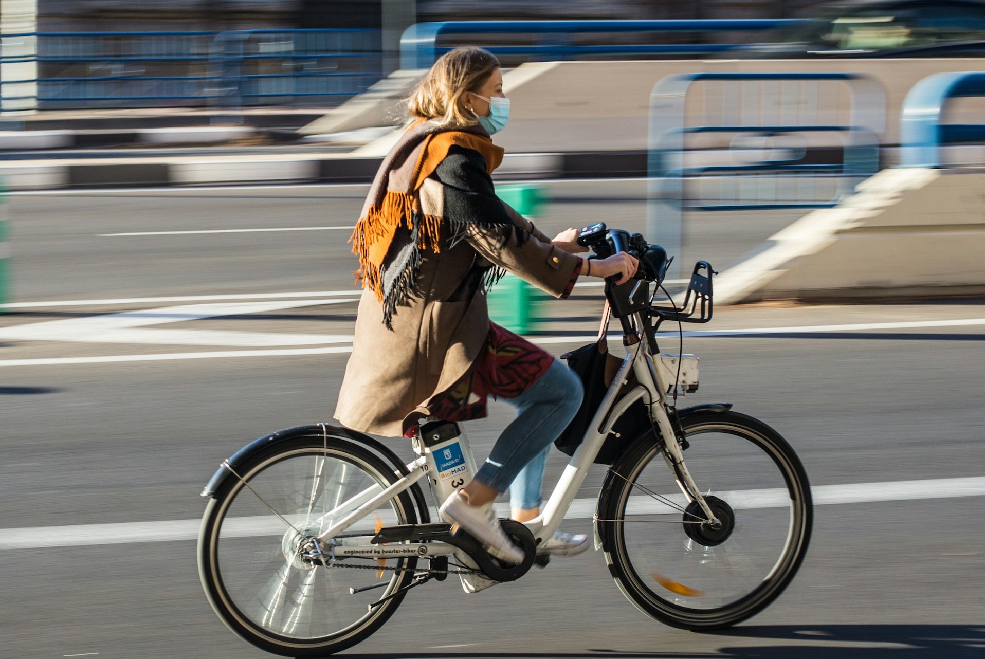 A woman wearing a facemask rides an e-bike in an urban setting.
