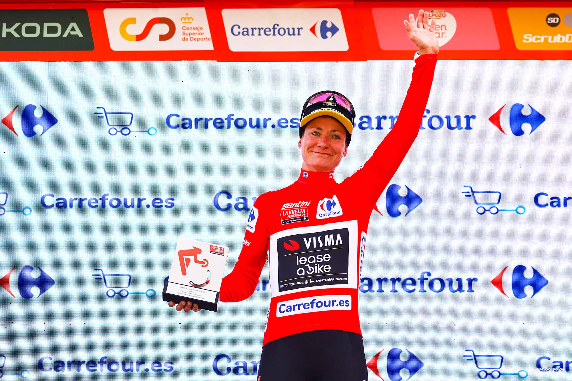 Marianne Vos raises her arm on the podium as she collects the red jersey for current race leader.