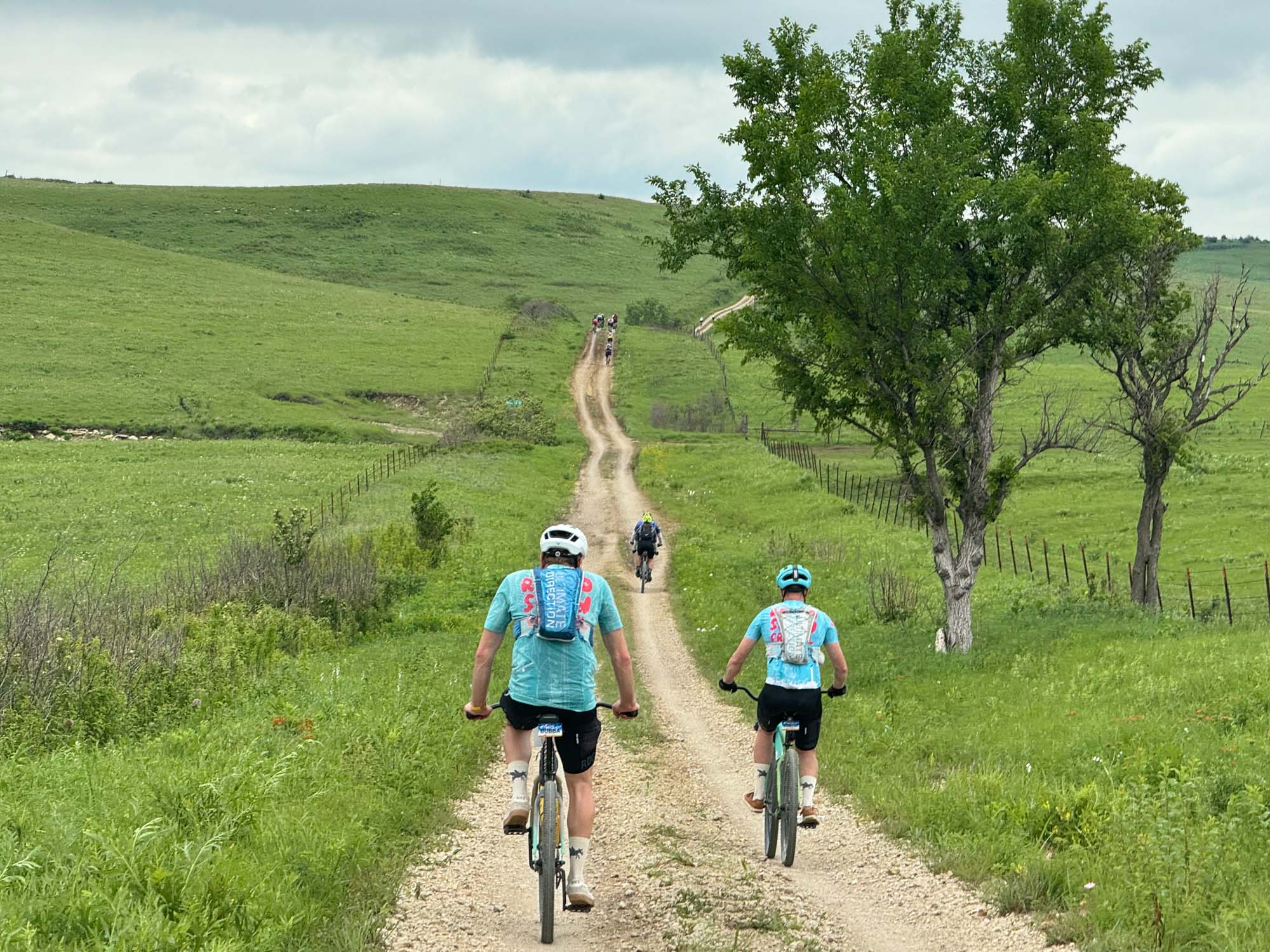 Two riders on a rough gravel road through rolling hills.