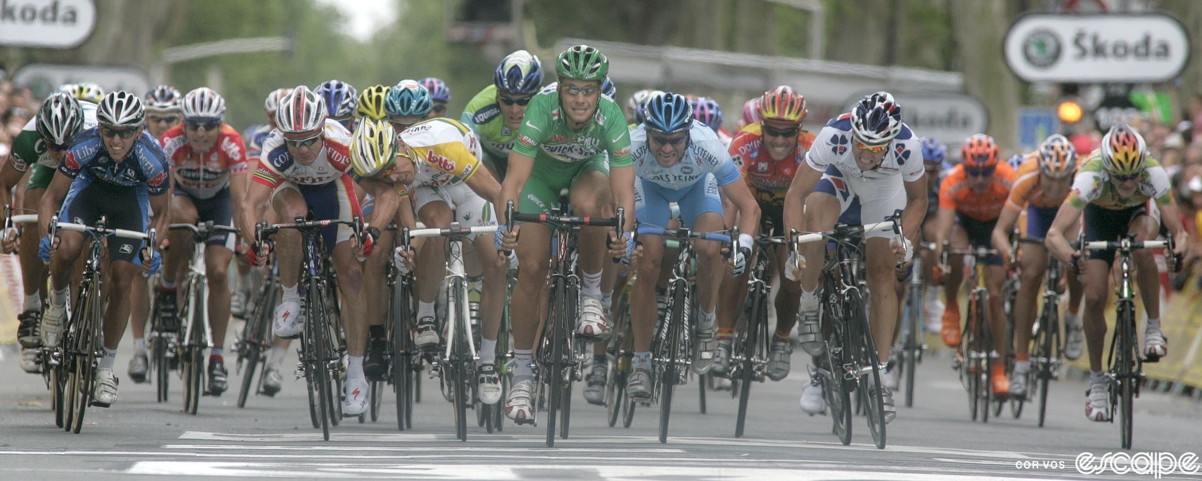 A wide-angle shot of a Tour de France sprint finish, with Australian sprinters Robbie McEwen and Stuart O'Grady tangling just before the line. McEwen leans far over his bike to headbutt O'Grady's left shoulder.