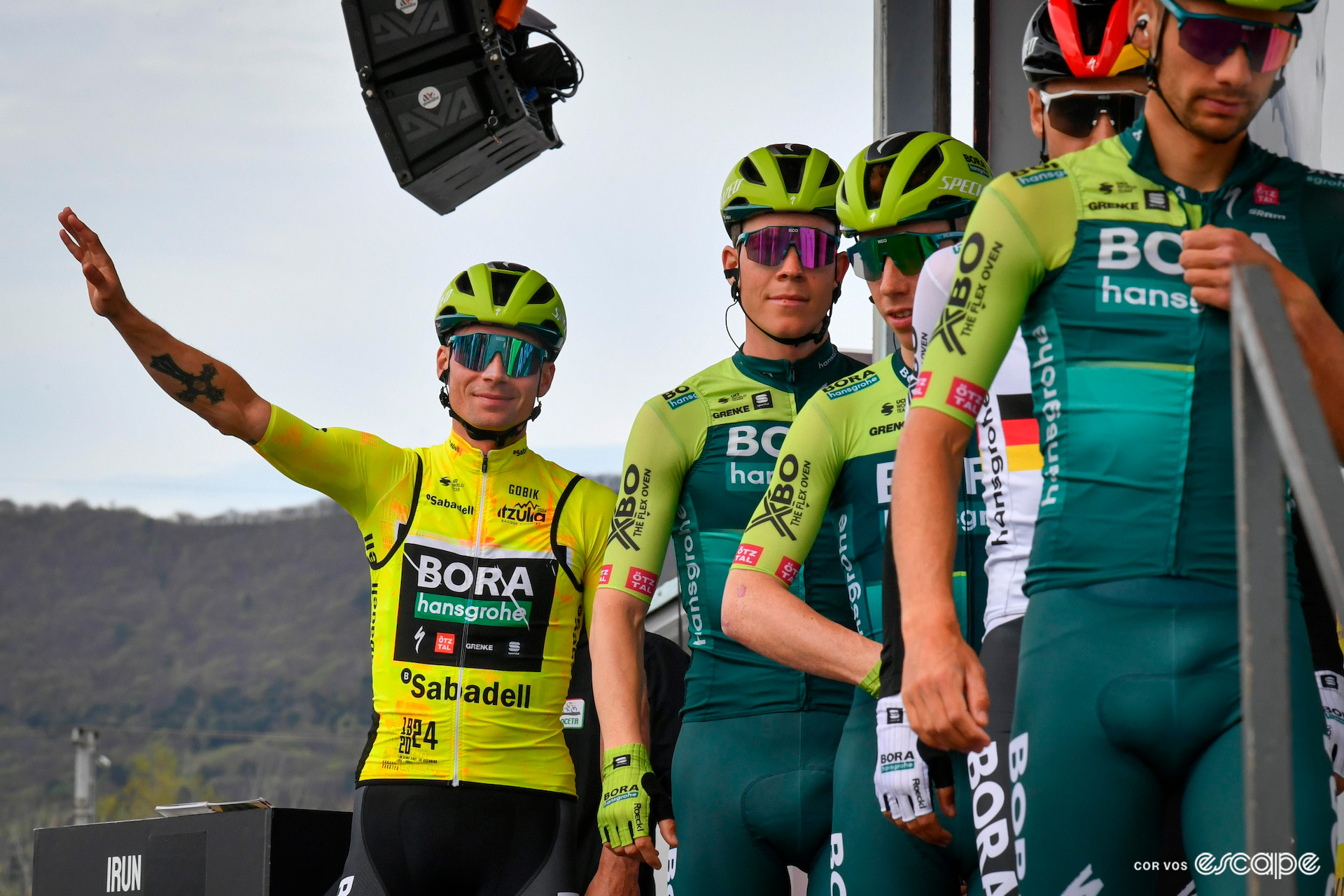 Primož Roglič in the yellow jersey waves to the crowd from the podium as his team leads the way off the stage at Itzulia Basque Country.