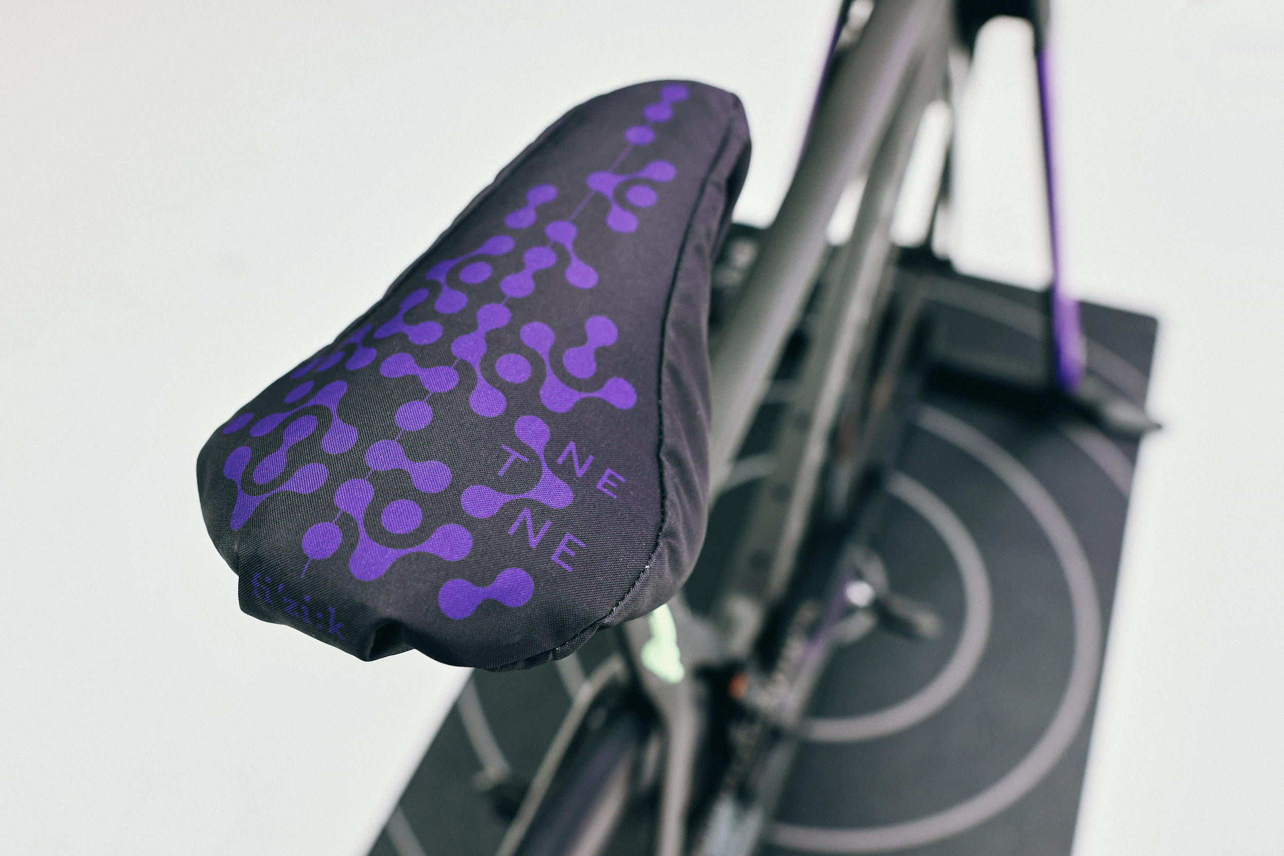 A pressure-mapping saddle cover sits on a bike seat during a fit session. The cover has purple dots that correspond to pressure sensors.