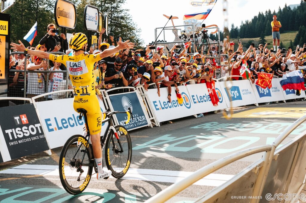 Tadej Pogačar throws his arms wide as he crosses the line to win stage 19 of the 2024 Tour de France.