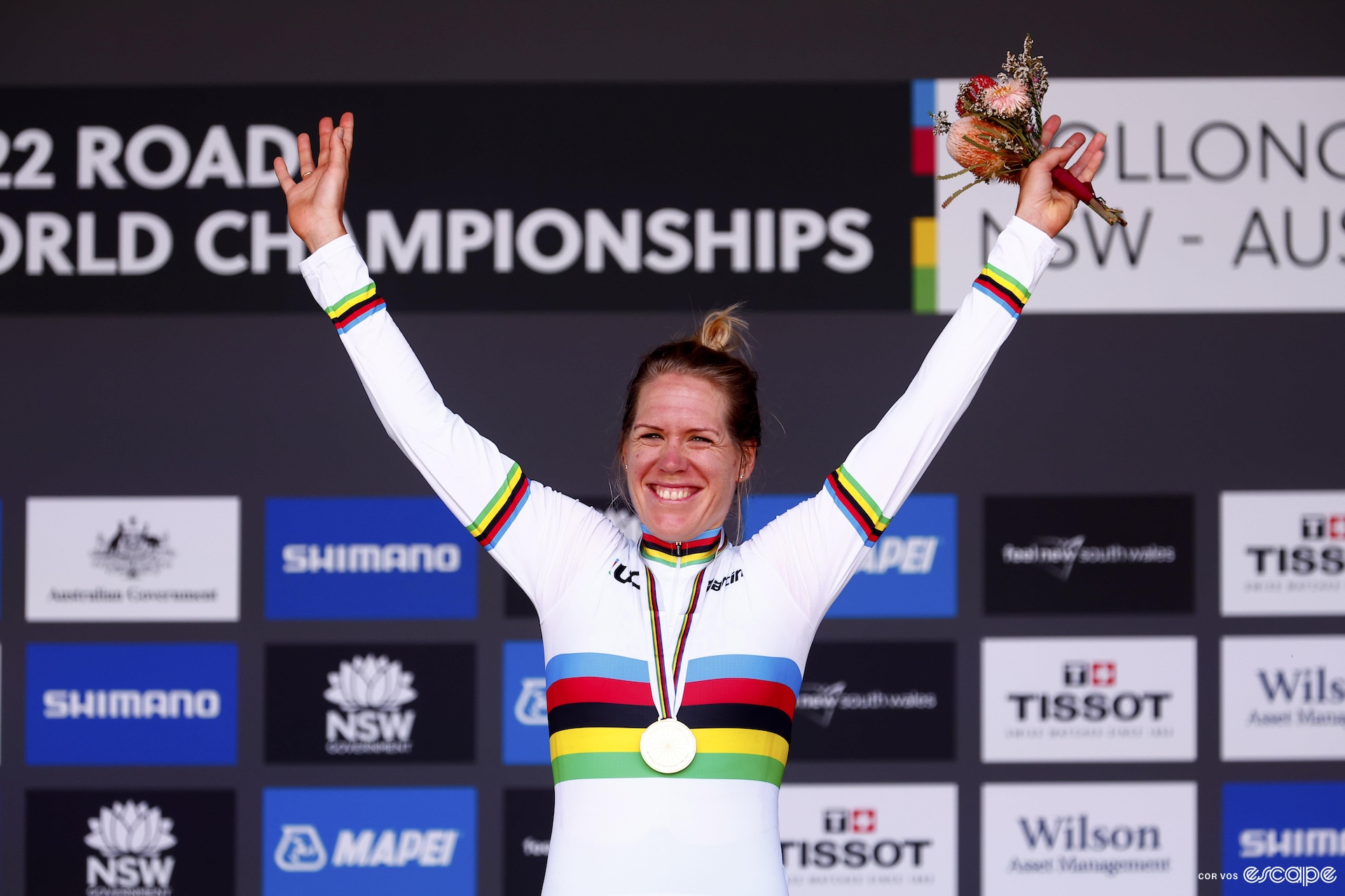 Ellen stands on the podium, arms in the air, in a brand new rainbow jersey. 