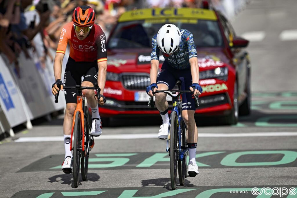 Carlos Rodríguez and Jonas Vingegaard cross the finish line on stage 4 of the 2024 Tour de France. Vingegaard's head hangs low as he slumps over the bike from the effort.