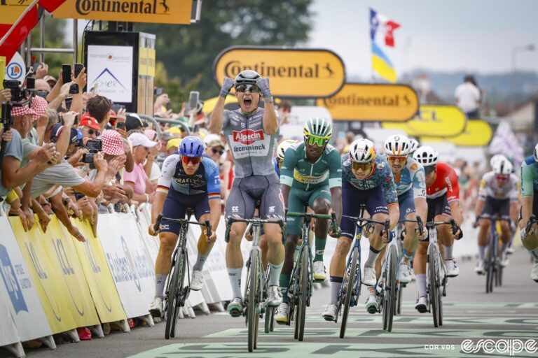 Jasper Philipsen punches both hands in the air in front of him as he wins stage 10 of the 2024 Tour de France. Biniam Girmay sits up just behind in second at the head of a small group of sprinters.