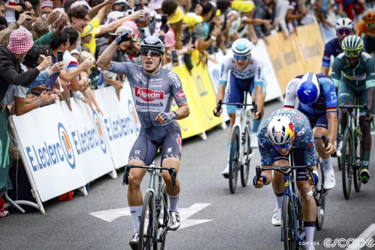 Jasper Philipsen punches the air as he crosses the line to win stage 13 of the 2024 Tour de France. To his left, Wout van Aert throws his bike forward in an unsuccessful attempt to win.