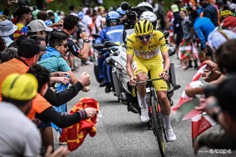 Tadej Pogačar in a yellow skinsuit climbs alone through the crowd towards the end of stage 14 of the 2024 Tour de France.
