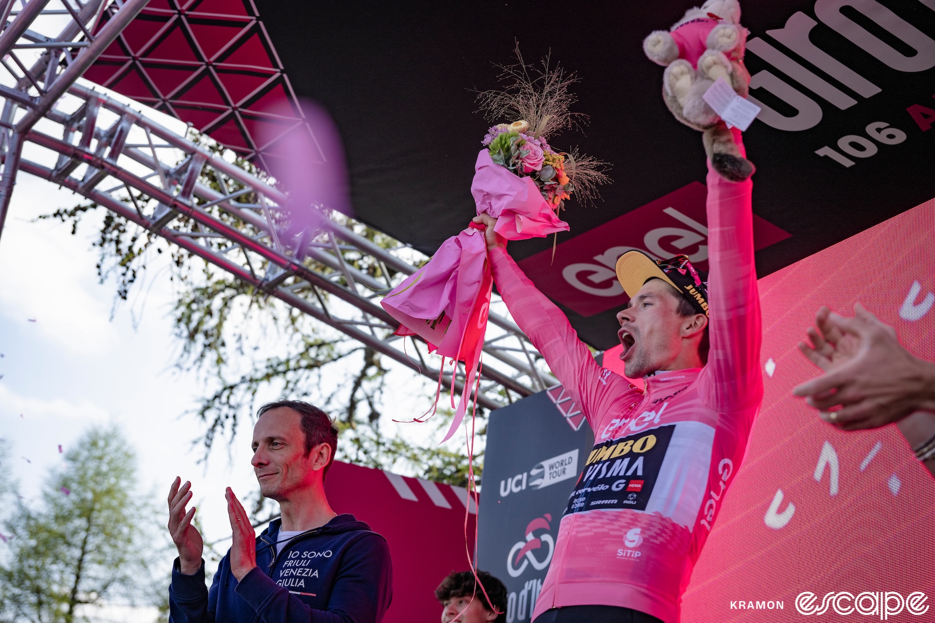 Primož Roglič lets out a roar as he raises both hands on the podium of stage 20 of the 2023 Giro d'Italia, after having just won the stage and overhauled Geraint Thomas for the pink leader's jersey.