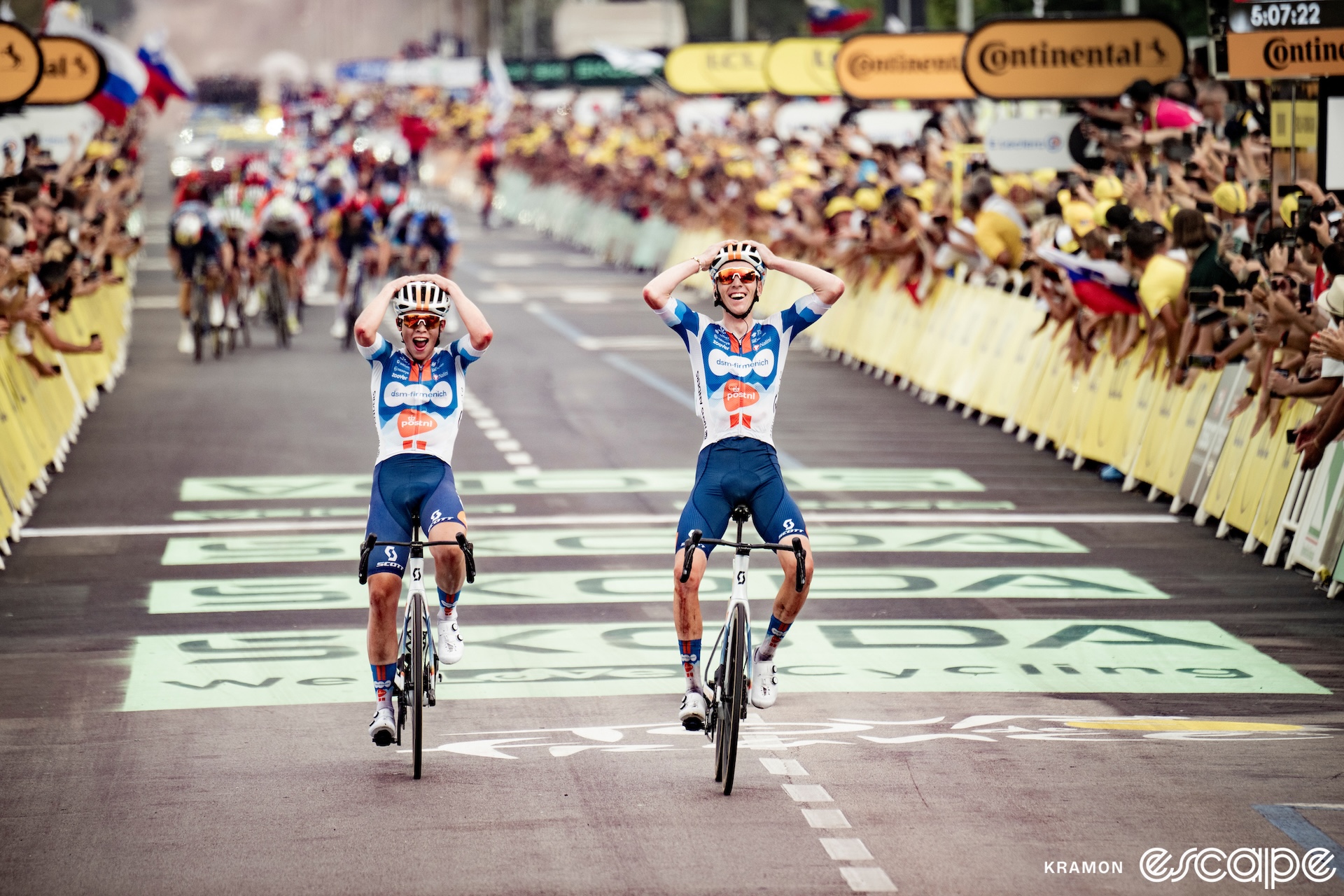 Frank van den Broeck and Romain Bardet simultaneously put their hands on their heads as they cross the line together to take stage 1 of the 2024 Tour de France. Behind, a hard-charging peloton has just failed to catch them.