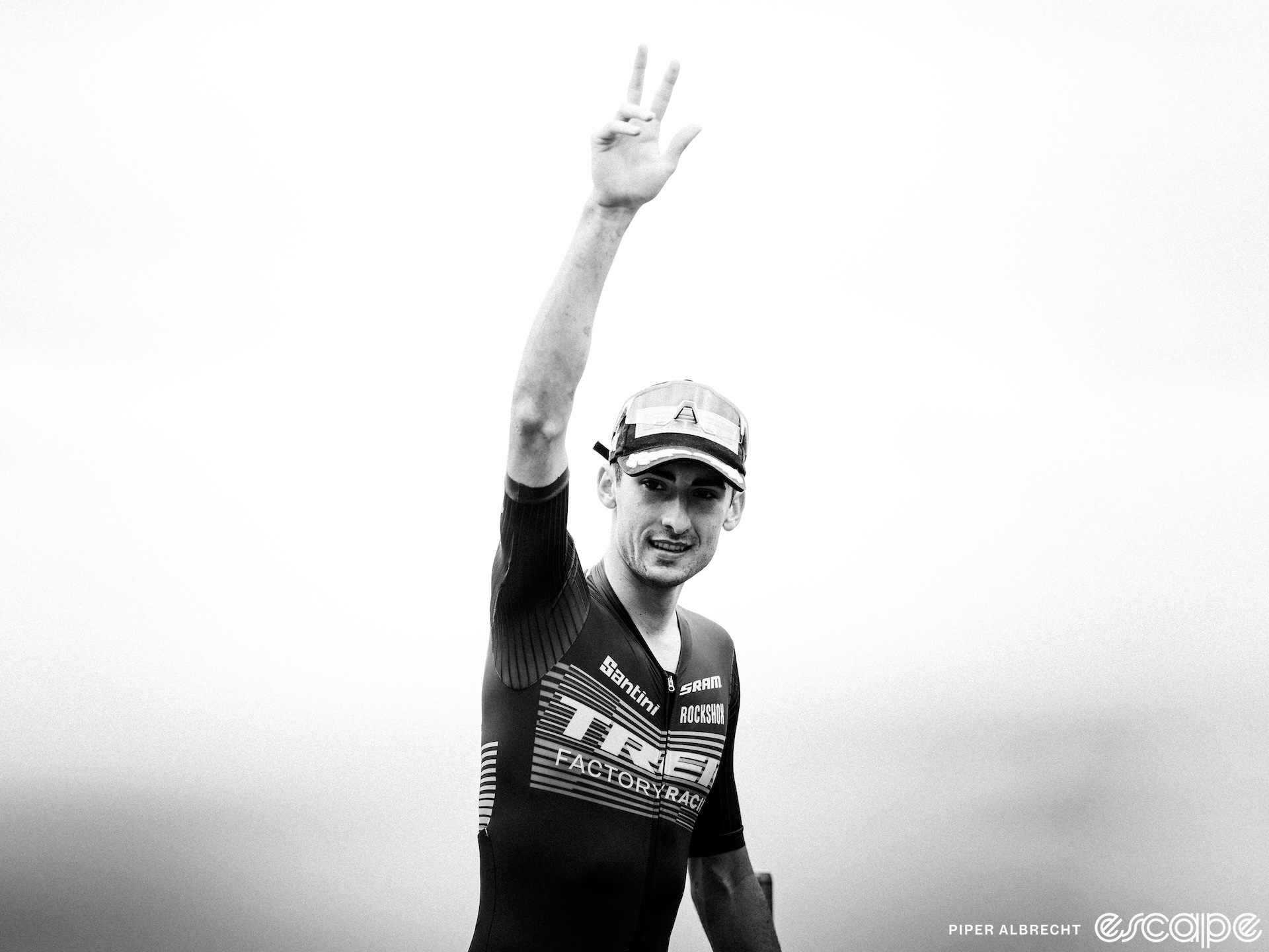 Riley Amos waves as he approaches the podium after winning the Crans-Montana World Cup. He is dressed in Trek factory kit and has an arm in the air in this black and white image.