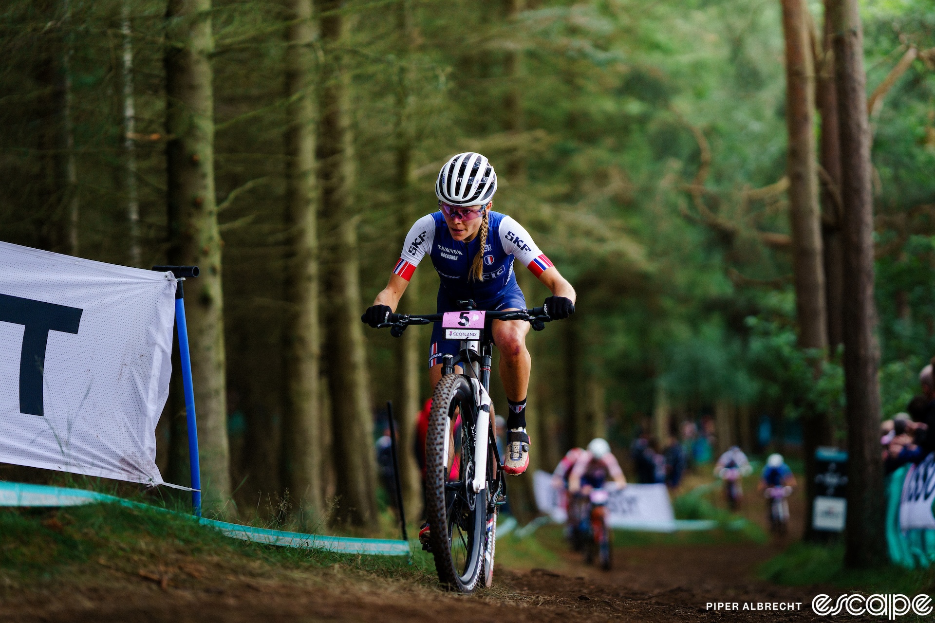 Loana Lecomte climbs an off-camber section in the woods at the World Championships in Glasgow, Scotland. Behind, you can just make out the blurry form of Puck Pieterse chasing.