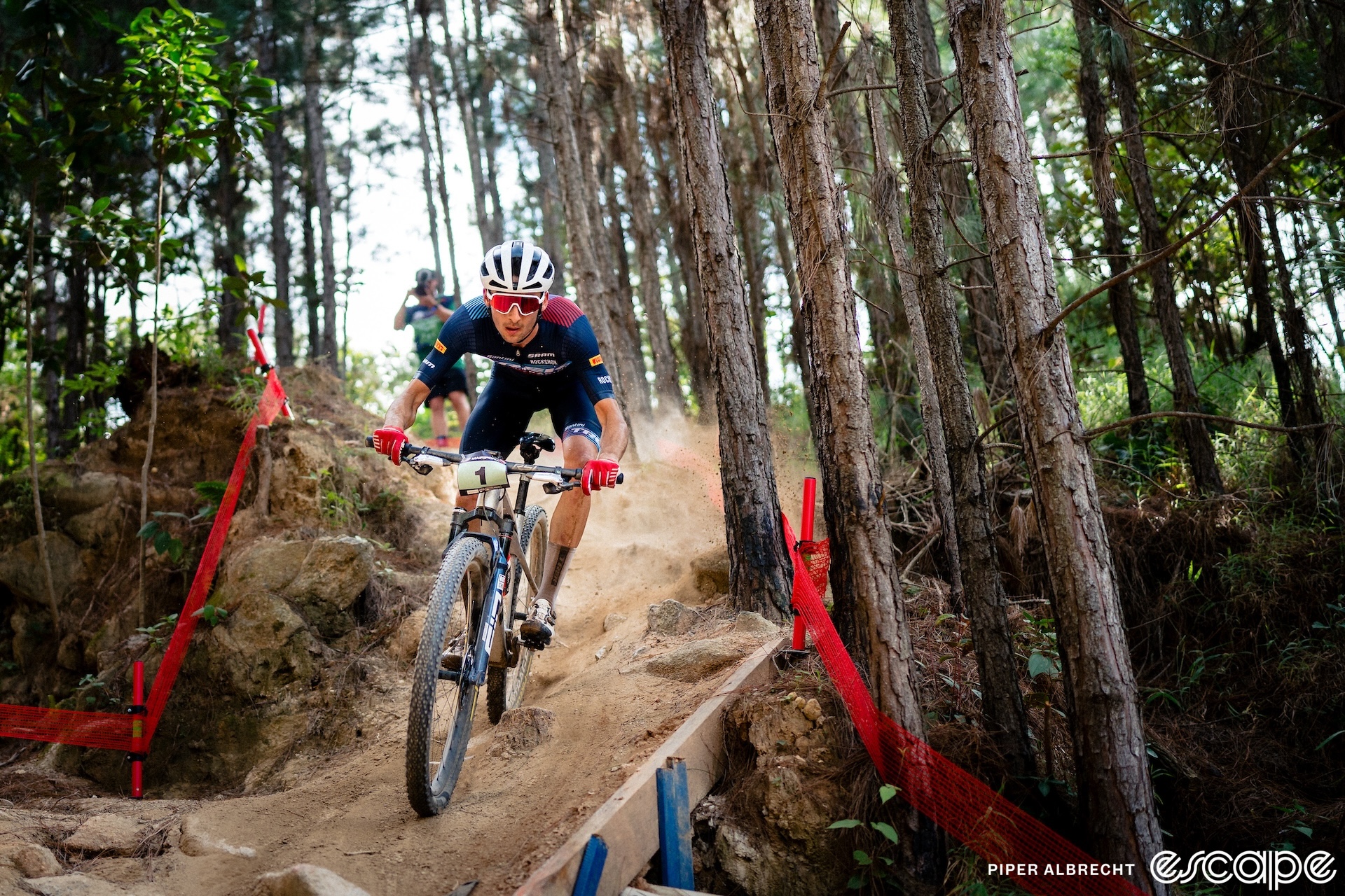 Riley Amos descends a dusty, rocky singletrack at a World Cup in Brazil. He's all alone, with an intense look of concentration and is in attack position on the bike as he looks ahead.