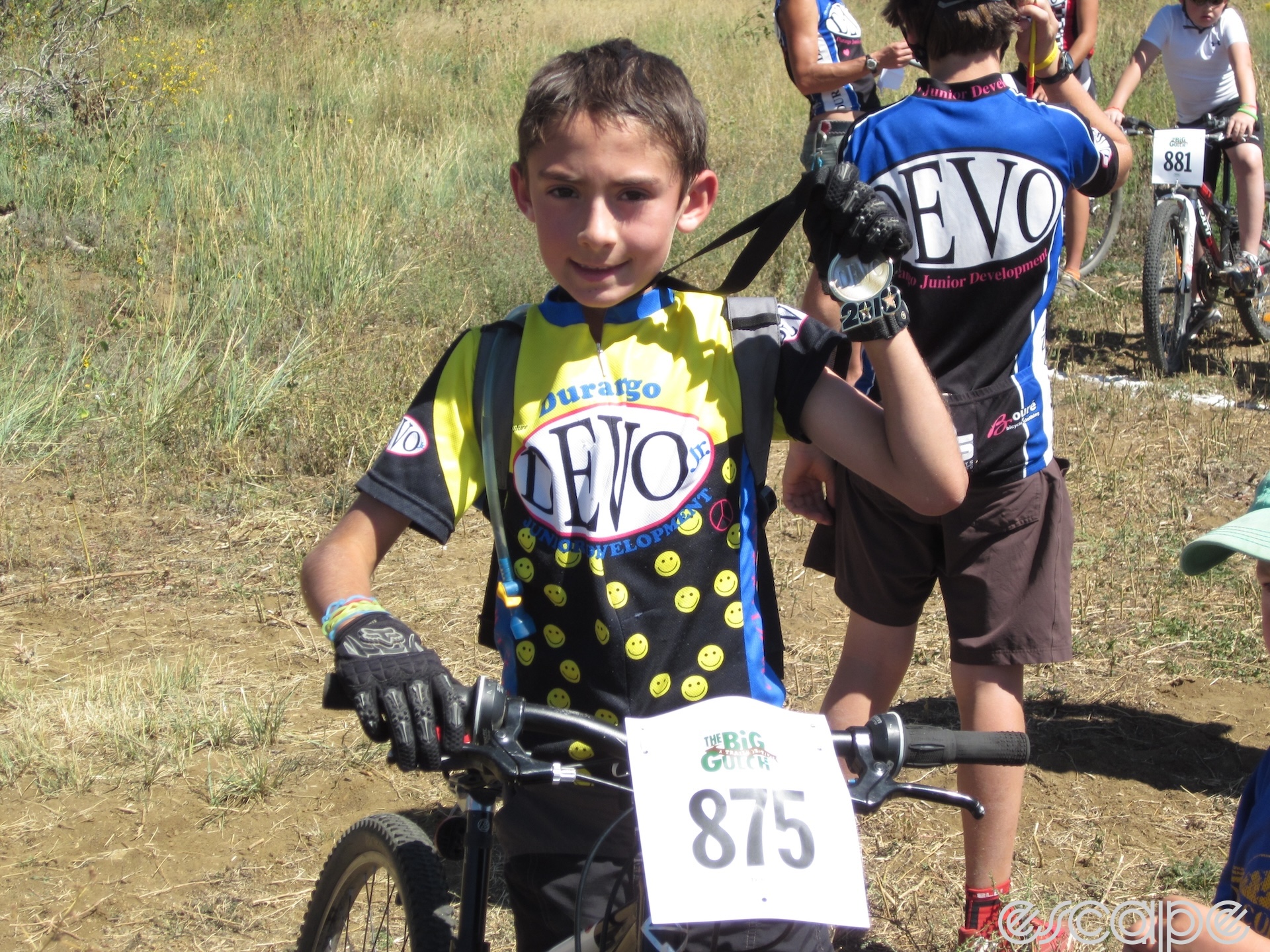 Riley Amos displays a medal for participating in a Devo race. He's just eight, and the sleeves of the Devo jersey he's wearing hang loosely around his skinny arms. He has a happy, determined expression.