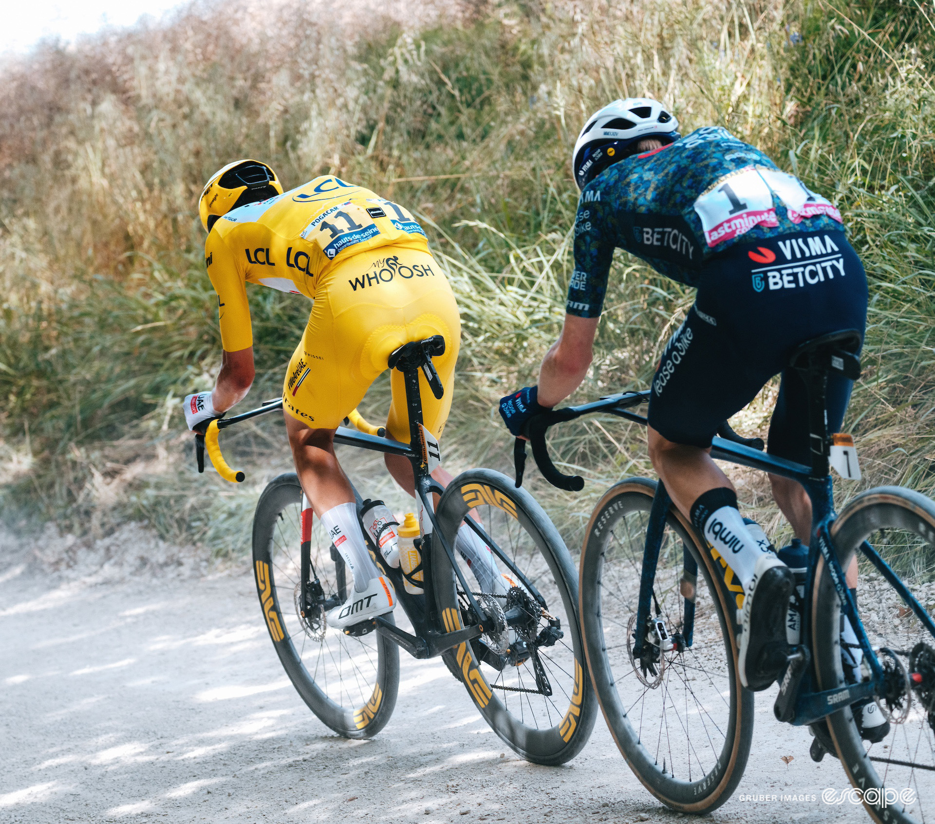 Seen from behind, Tadej Pogačar in the yellow jersey leads Jonas Vingegaard on a gravel sector during stage 9 of the 2024 Tour de France.