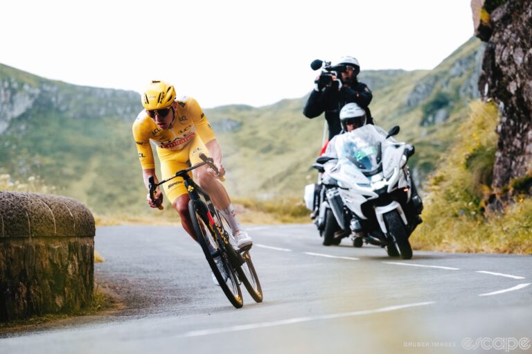 Tadej Pogačar attacks down a descent during stage 11 of the 2024 Tour de France. He's all alone, trailed by only a TV camera moto through a twisty corner.