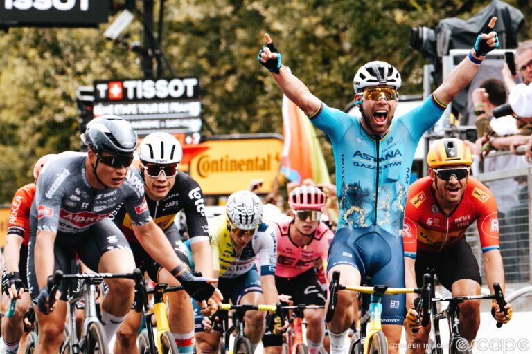 Mark Cavendish sits up and raises his hands as he wins a record-setting 35th Tour de France stage. His mouth is open wide in a euphoric shout.