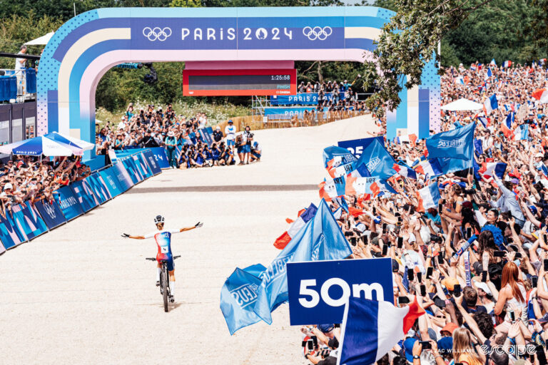 Pauline Ferrand-Prévot seen from behind as she crosses the finish line, her arms thrown wide, as she wins Olympic mountain bike gold in front of a huge home crowd.