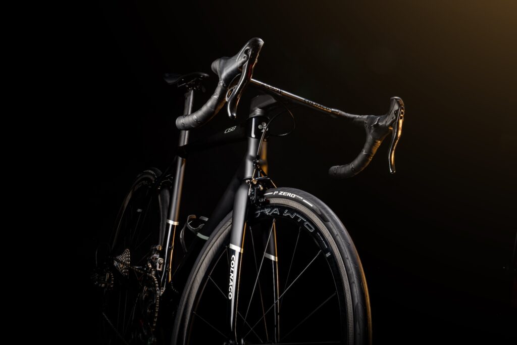 Colnago's rim-brake C68 road bike. It's shown all in black, with black wheels, tires and handlebar tape, looming out of a black background. The light fades out the rear third of the bike so it looks like it's emerging from darkness.